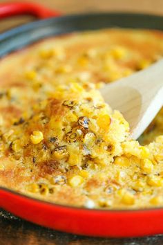 a wooden spoon scooping corn out of a red casserole dish on a table