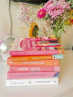 a stack of books sitting on top of a table next to a vase filled with flowers