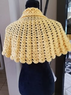 a yellow crocheted shawl on display in front of a mirror and door