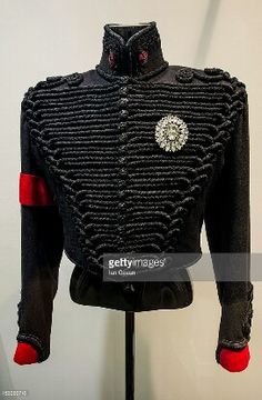 an old black jacket with red buttons on the chest and sleeves is displayed in a museum