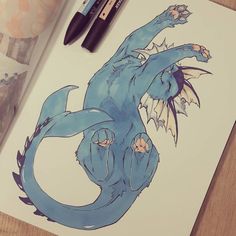 a drawing of a blue dragon sitting on top of a table next to markers and pens