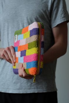 a person holding a multicolored purse in their hands and wearing a gray shirt