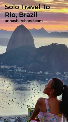 a woman sitting on top of a hill looking at the ocean and mountains in rio, brazil