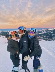 three people standing on top of a snow covered slope wearing skis and goggles