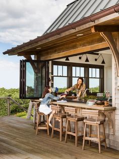 two women sitting at a bar on the back deck of a house with an outdoor kitchen