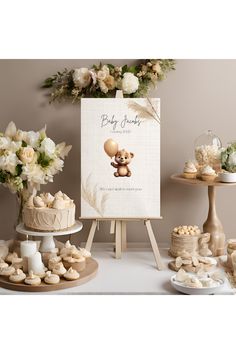 a baby shower sign surrounded by desserts and flowers on a white table with an easer