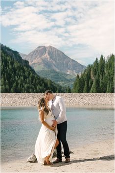 a man and woman standing next to each other on a beach in front of mountains