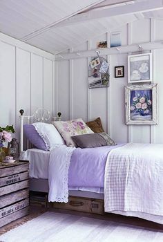 a bedroom with white walls and pictures on the wall above the bed, along with an old chest of drawers