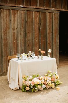 a table with flowers and vases on it in front of a wooden wall at a wedding reception