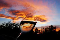 a glass of wine sitting on top of a table next to a sunset behind it