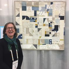 a woman standing next to a quilt hanging on a wall