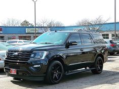 a black suv parked in front of a building with other cars and trucks behind it