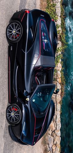 an aerial view of a black sports car parked on the side of a road next to water