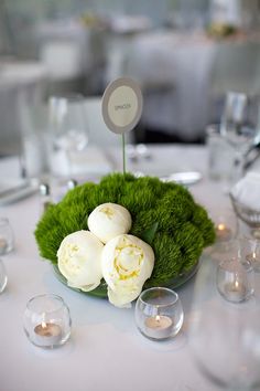 an arrangement of white flowers and greenery on top of a table with silverware