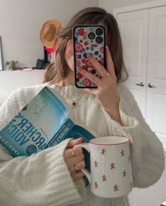 a woman taking a selfie while holding a book and coffee mug in her hands