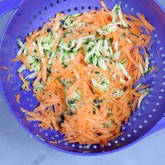 a blue colander filled with shredded carrots and broccoli florets