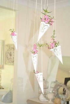 three white paper cones with pink flowers hanging from the ceiling in front of a mirror