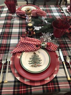 the table is set for christmas dinner with red and white plates, silverware, and plaid napkins