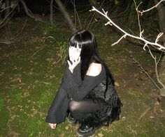 a woman sitting on the ground with her hands to her face while wearing black clothing