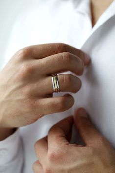 a person wearing a gold ring and white shirt with their hands on the other hand