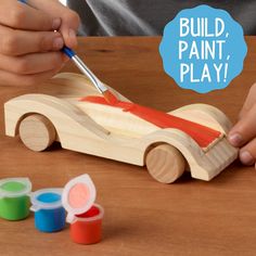 a person painting a wooden toy car with red paint on it's body and the words build, paint, play below