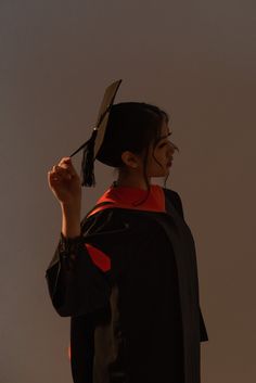 a woman wearing a graduation gown and holding up her hat with one hand in the air