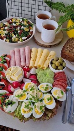 an assortment of food is displayed on a table with utensils and cups in front of it