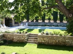 an outdoor swimming pool surrounded by stone walls and trees with chairs around the pool area