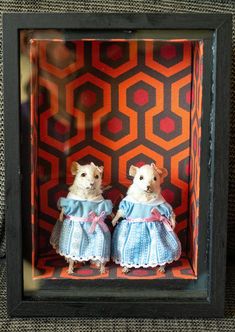 two stuffed animals are dressed in blue and white outfits, sitting inside a shadow box