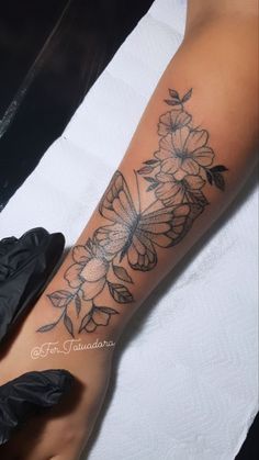 a woman's arm with a butterfly and flowers tattoo on it