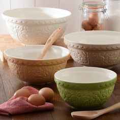 four bowls and two spoons on a table with eggs in the bowl next to them