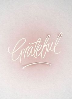 the word grateful written in cursive writing on a white paper with a pink background