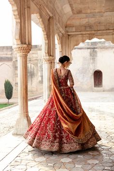 a woman in a red and gold wedding dress standing on a stone walkway with arches