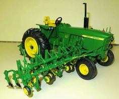 a green tractor with yellow wheels is on the floor in front of a white wall