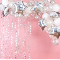 balloons and stars are hanging from the ceiling in front of a pink wall with silver confetti