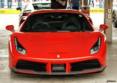 the front end of a red sports car parked in a garage with people looking at it