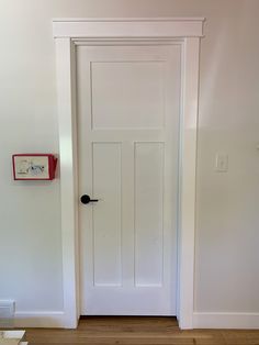 an empty room with a white door and wooden floor in front of the door is a clock on the wall