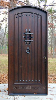 a large wooden door sitting on the side of a sidewalk in front of a tree