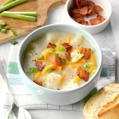 a bowl of potato soup with bacon and green onions in it next to a loaf of bread