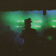 a man with dreadlocks standing in front of green lights