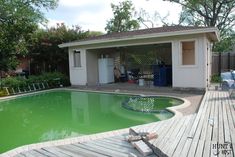 a pool with green water in the middle of a wooden decked area next to a house