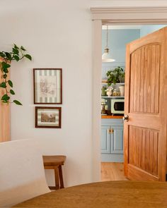 an open door leading to a kitchen with blue cabinets and white walls, along with a wooden dining table