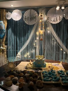 a table topped with lots of cupcakes next to a window covered in sheer curtains