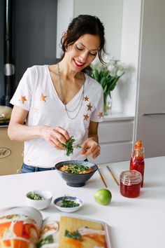 a woman preparing food in a bowl on top of a white kitchen counter next to an open book