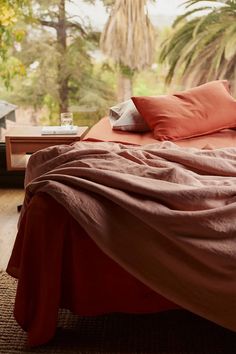 an unmade bed with red sheets and pillows on top of it in front of a window