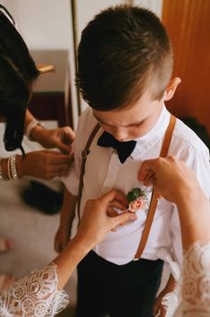 a man in a white shirt and bow tie is fixing another mans suspender on his wedding day