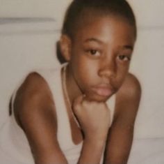 a young boy sitting on top of a bed next to a white pillow and blanket