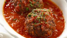 two meatballs covered in marinara sauce and garnished with parsley