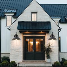 a white house with black trim and two lights on the front door is lit up at night