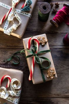 three wrapped presents with ribbons and bows on top of a wooden table next to spools of thread